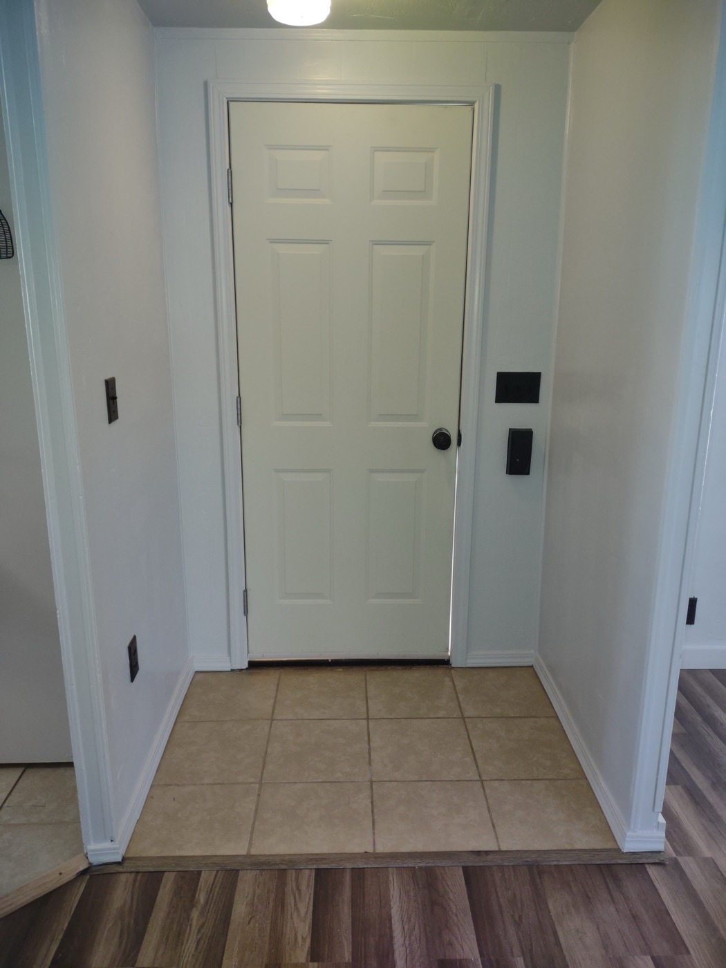 Clean white entryway with new tile floor and LVP wood-look flooring in adjacent room