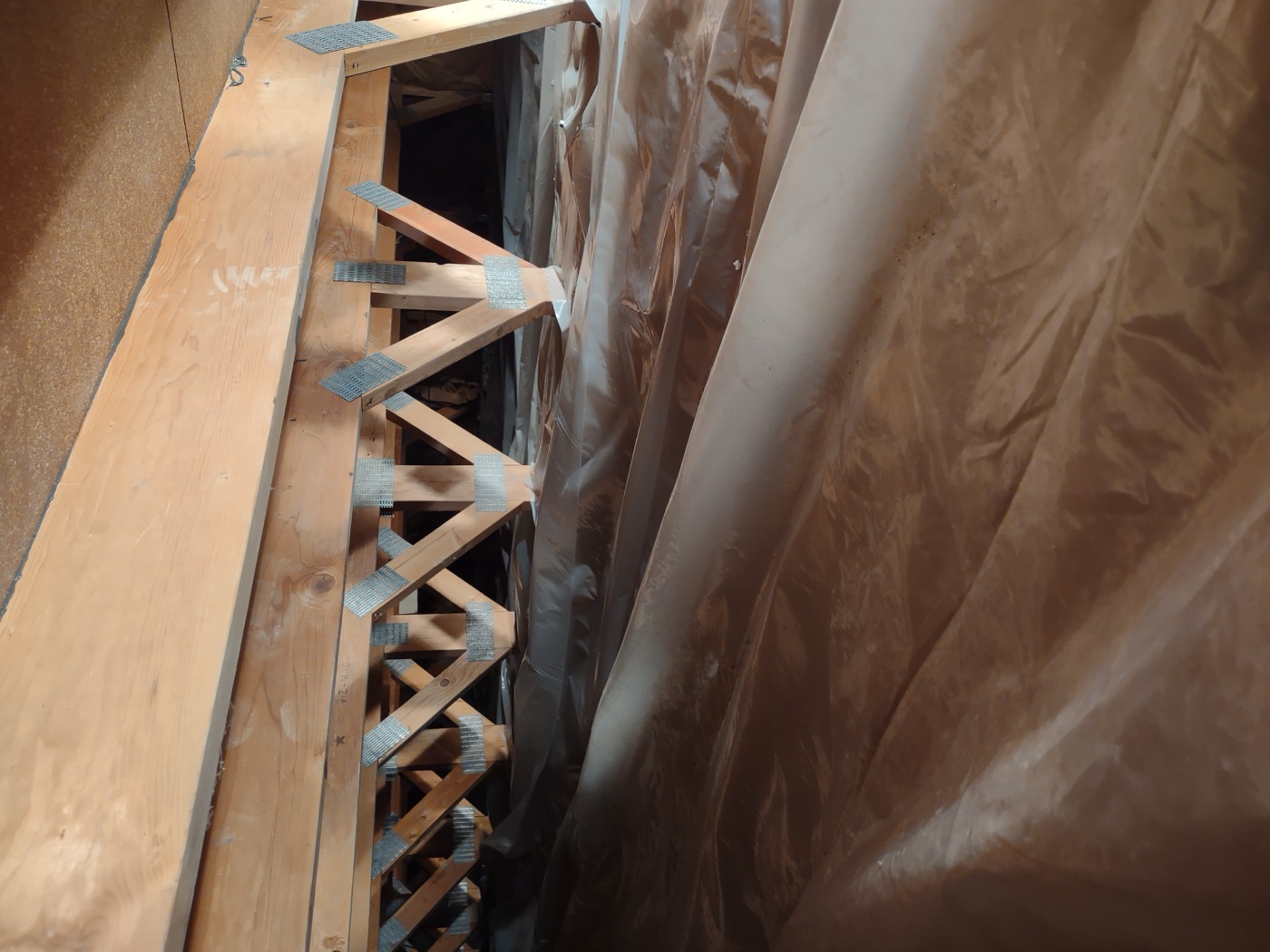 Brown poly vapor barrier sheeting installed against crawlspace walls with floor trusses visible above